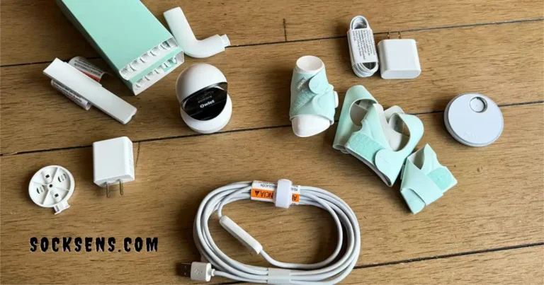 A photo showing the components of the Owlet Sock Monitoring System, including the sock sensor, base station, camera, power adapters, and cables.